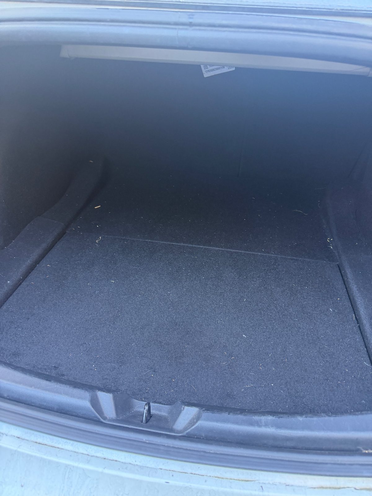 Boot of a white Tesla Model 3 before detailing, with dust and fibres on the carpet