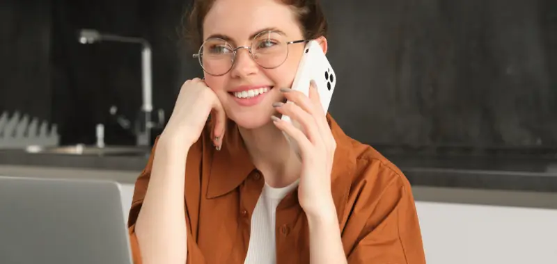 Smiling woman talking on a phone with a laptop open in front of her