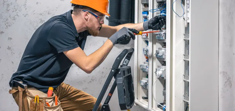 Electrician in an orange hard hat working on a large commercial electrical panel