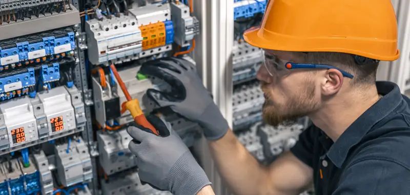 Electrician in an orange hard hat and safety glasses working inside a breaker panel