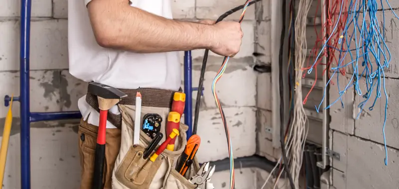 Electrician with a loaded tool belt holding bundled wires on a new construction site
