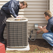 Two HVAC technicians working on an outdoor unit