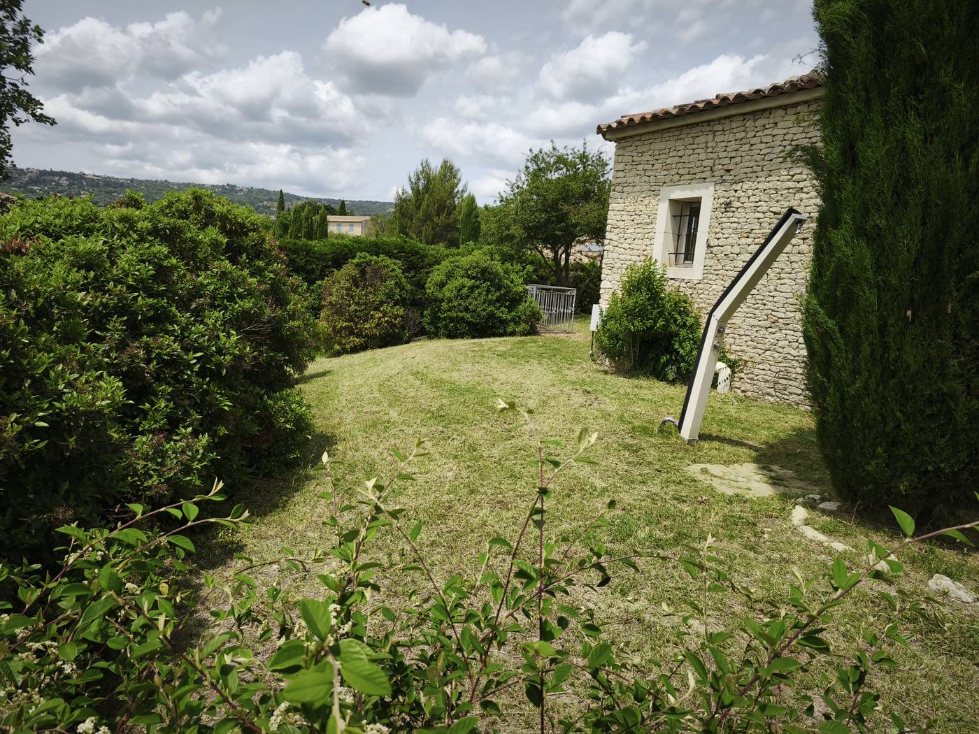 Pelouse tondue devant un mas en pierre et cyprès de Provence