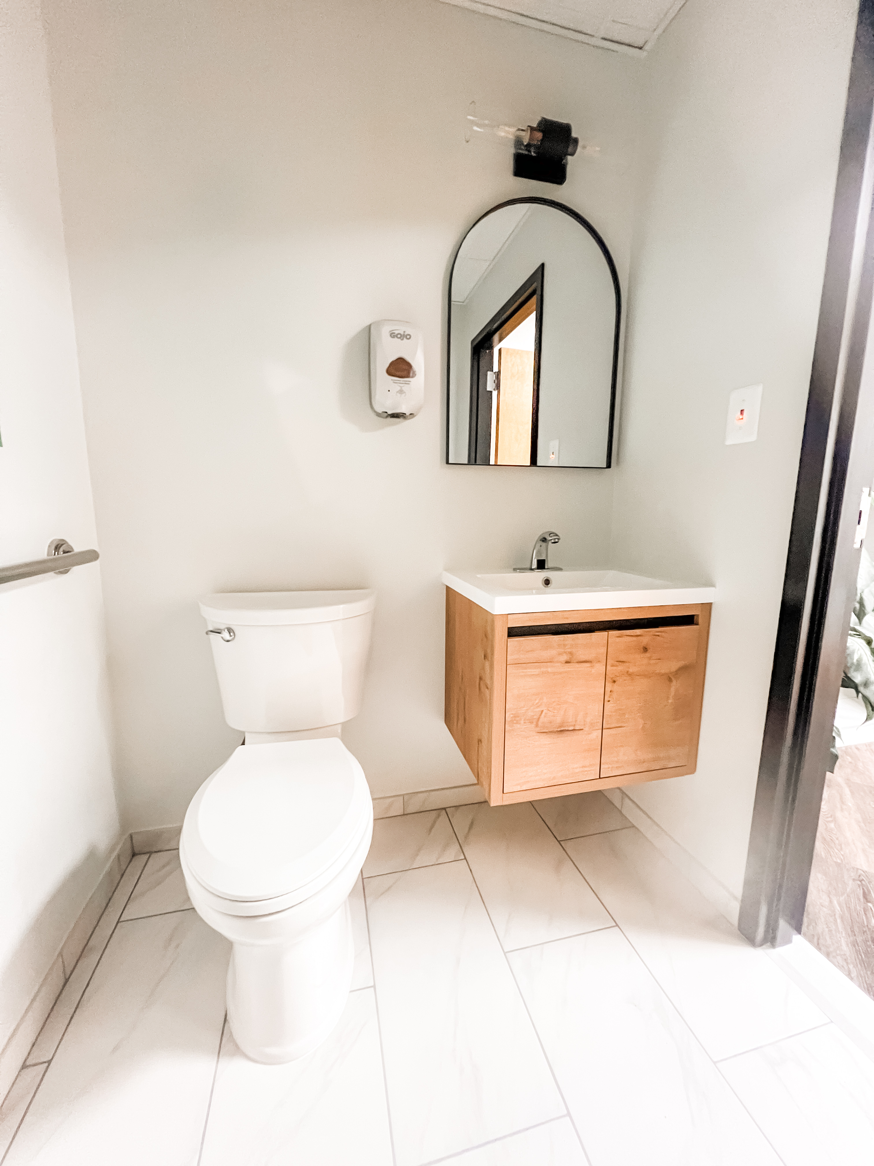 Small bathroom renovation with floating wood vanity, modern fixtures, and black framed mirror
