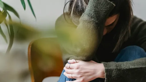 Person sitting curled up with their head resting on their knees