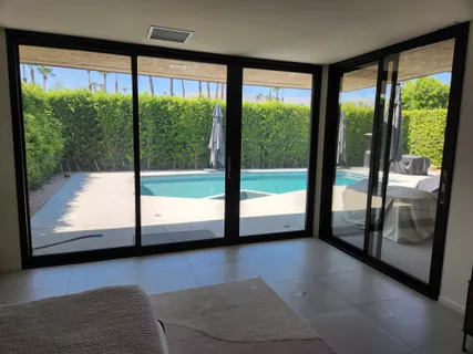 Interior of a desert home looking out through floor-to-ceiling sliding glass doors to a pool, with film on the glass.