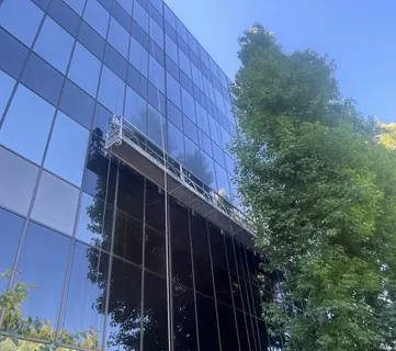 A suspended work platform positioned against the glass curtain wall of a multi-storey office building.