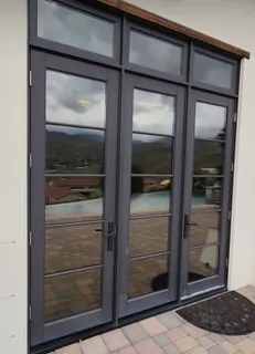 Tinted French doors opening onto a paved terrace, with a valley and hillside view beyond.