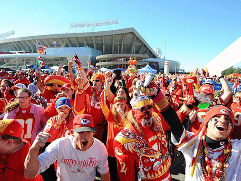 A vibrant crowd of KC Current fans dressed in light blue and red, waving scarves and flags in support of their team on game day. Perfect energy for KC Current Game Day Transportation, ensuring seamless travel to the stadium for fans.
