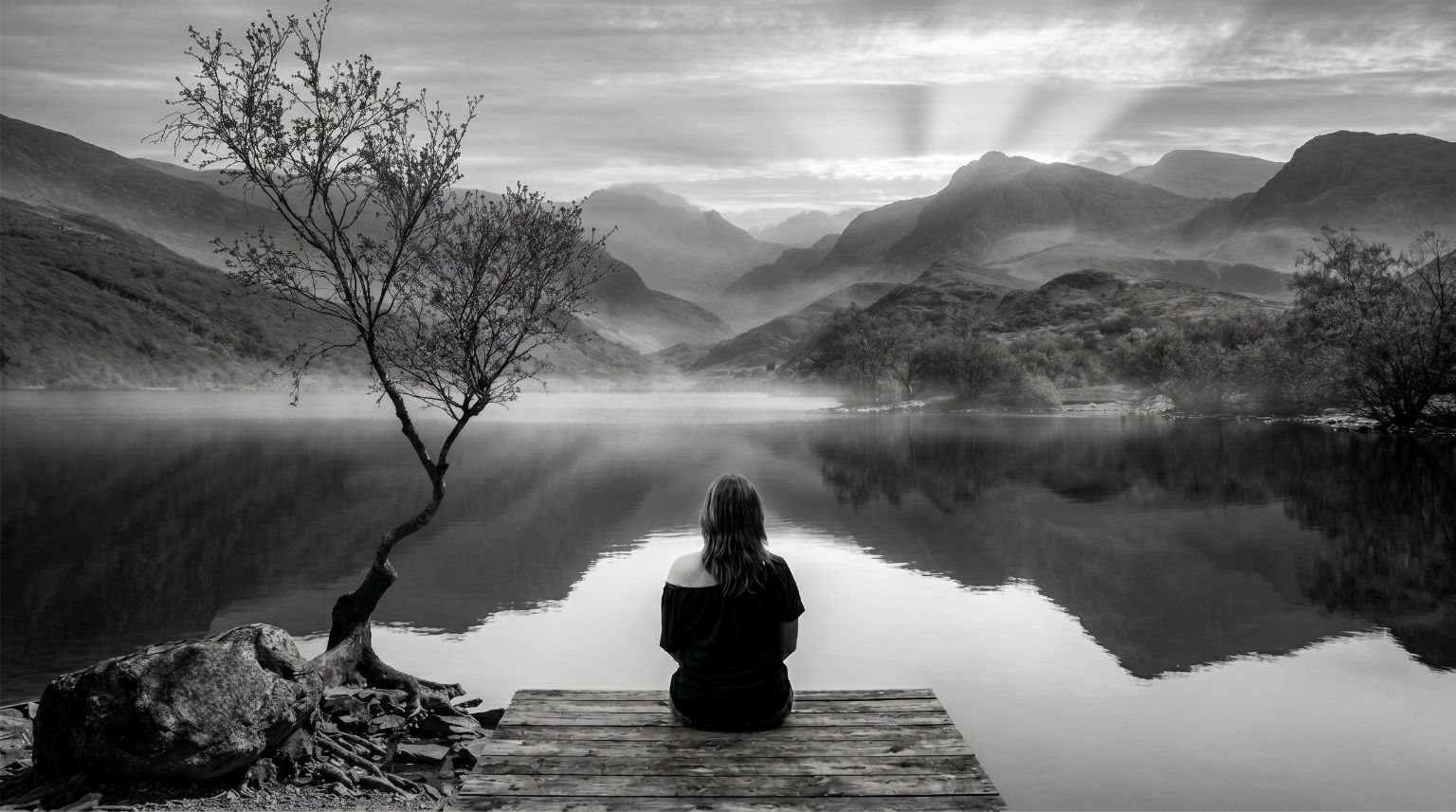 A woman looking out across a lake surrounded by a forest at dawn