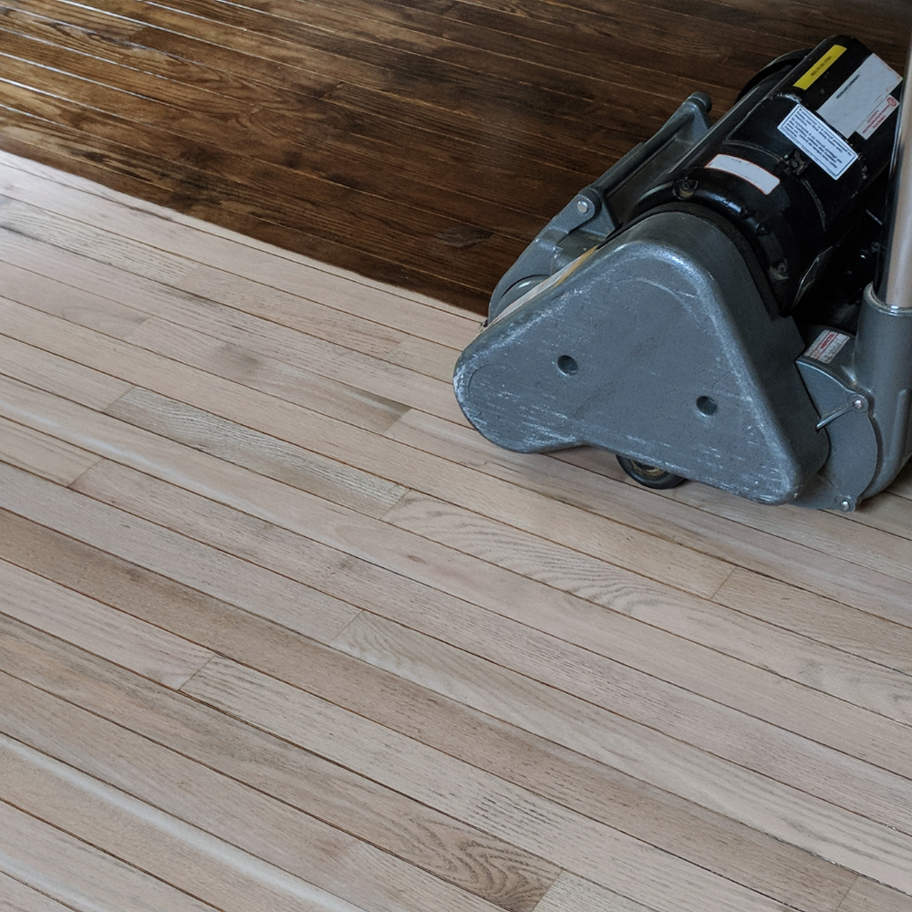 Hardwood floor refinishing in progress, showcasing a floor sander transitioning unfinished light wood to a polished dark stain.