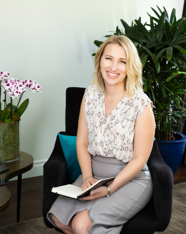 Photo of Mandi Ellefson seated in a black armchair holding an open journal.