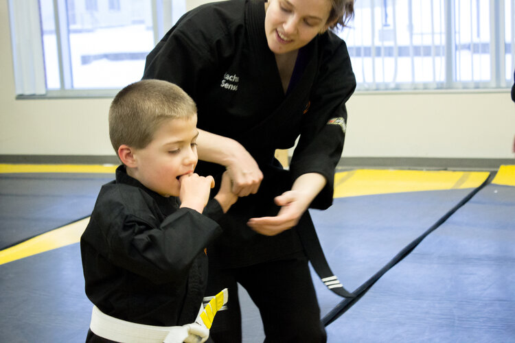 Special needs child being guided on the floor of the dojo by an instructor