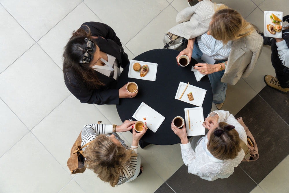 A small group seated around a table in a calm, upscale setting. One person is mid-conversation, while others listen. Subtly, the depth of field reveals additional figures in the background—slightly blurred—suggesting that what begins in a small, trusted space extends outward into something much larger. A small group seated around a table in a calm, upscale setting. One person is mid-conversation, while others listen. Subtly, the depth of field reveals additional figures in the background—slightly blurred—suggesting that what begins in a small, trusted space extends outward into something much larger.