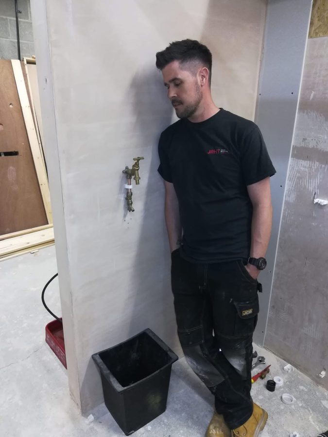 Rob Davis in work clothes on a job, stood by a newly fitted outside tap