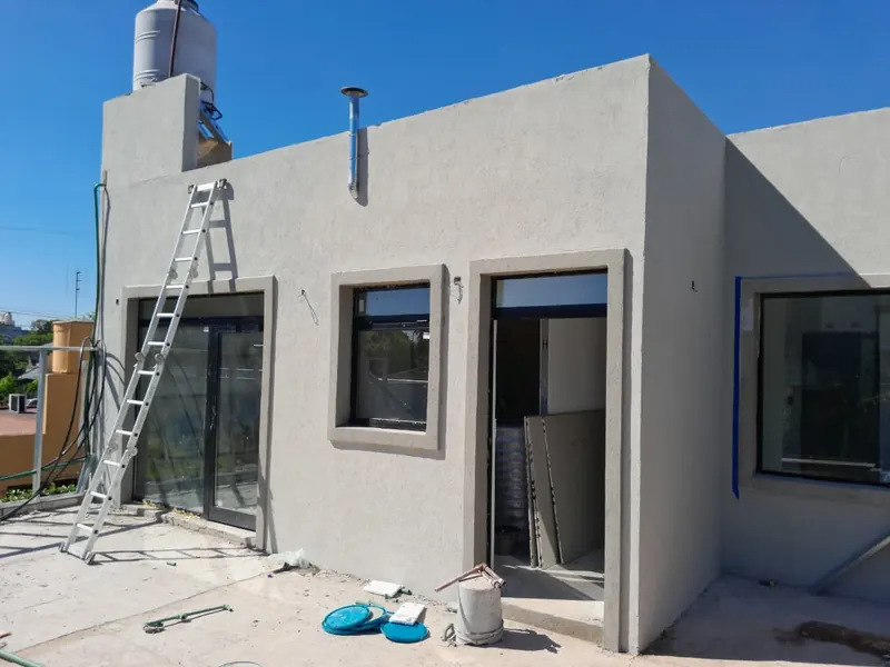 Planta alta en obra con revoque exterior terminado, escalera de aluminio y aberturas colocadas.