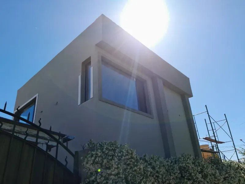 Esquina de vivienda de dos plantas con ventanales, vista desde abajo a contraluz del sol.