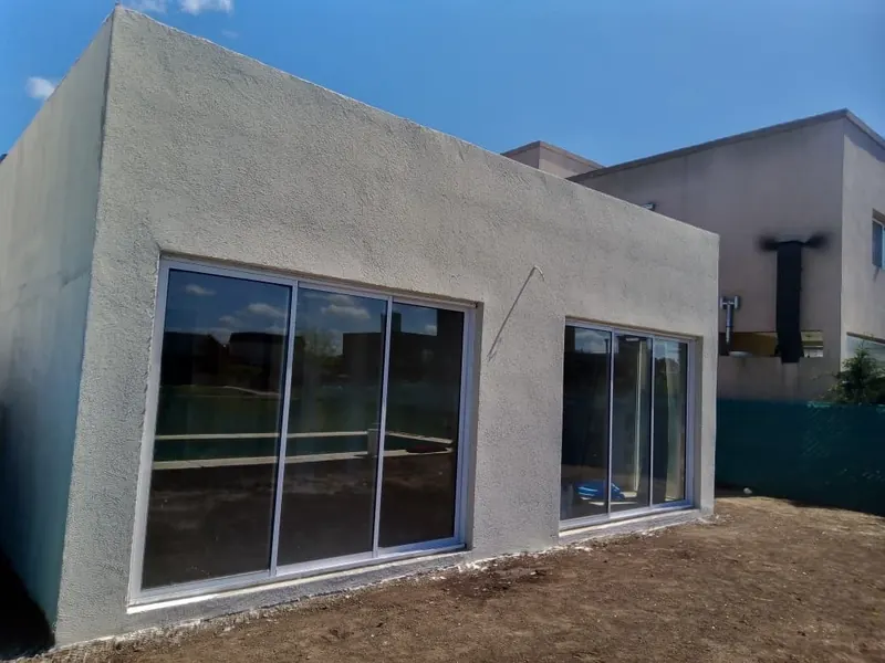 Volumen de una planta en gris claro con ventanales corredizos de aluminio bajo cielo azul.