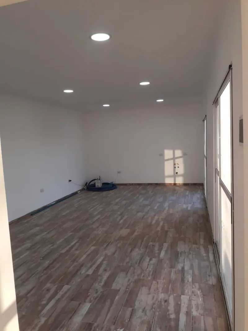 Ambiente amplio con piso símil madera, luces embutidas y puerta ventana lateral.