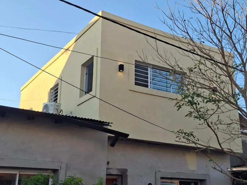 Planta alta en tono arena con una ventana enrejada y un aplique de pared, bajo cielo azul.