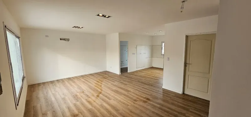 Ambiente amplio terminado, con piso símil madera, paredes blancas y luz natural.