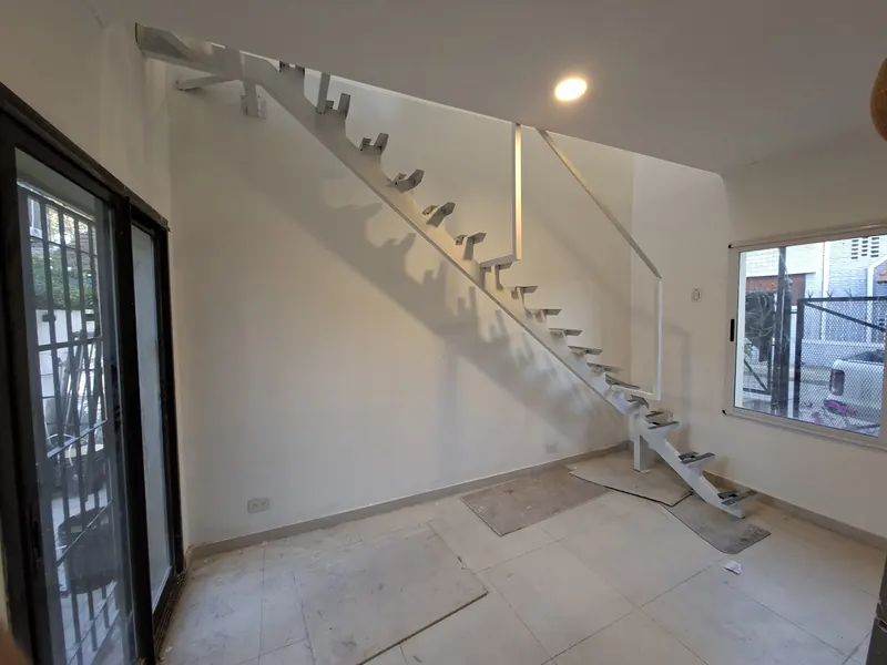 Escalera de un tramo con peldaños volados y baranda metálica blanca junto a un muro claro.