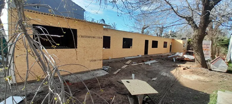 Muros de una vivienda en obra revestidos con placas de madera, con aberturas para ventanas y puertas.