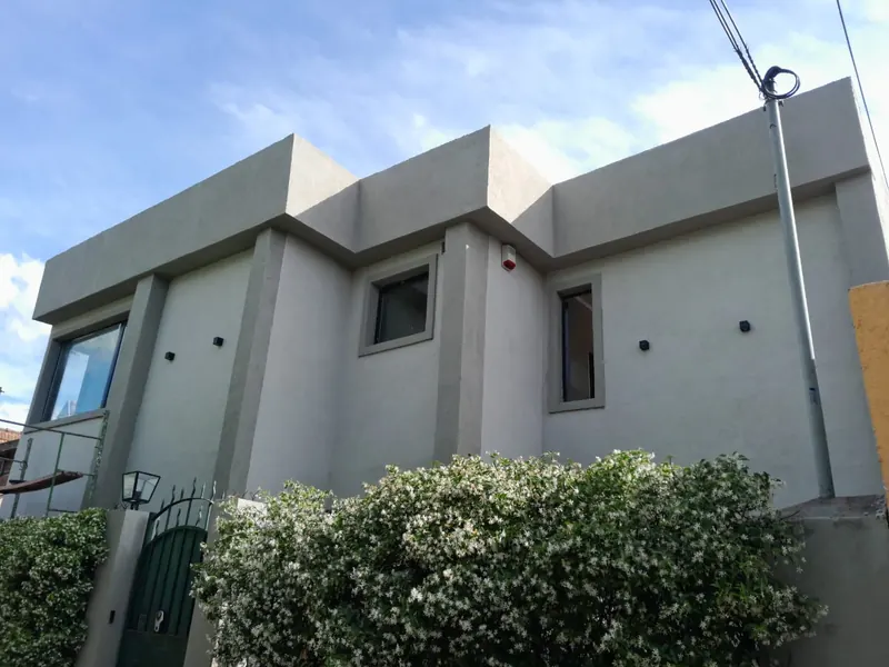 Fachada de dos plantas con revoque texturado gris claro y marcos de ventanas en gris más oscuro.