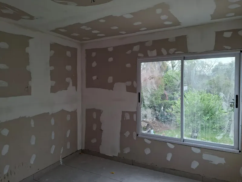 Dormitorio en obra con placas de yeso de juntas masilladas y ventanal hacia el jardín.