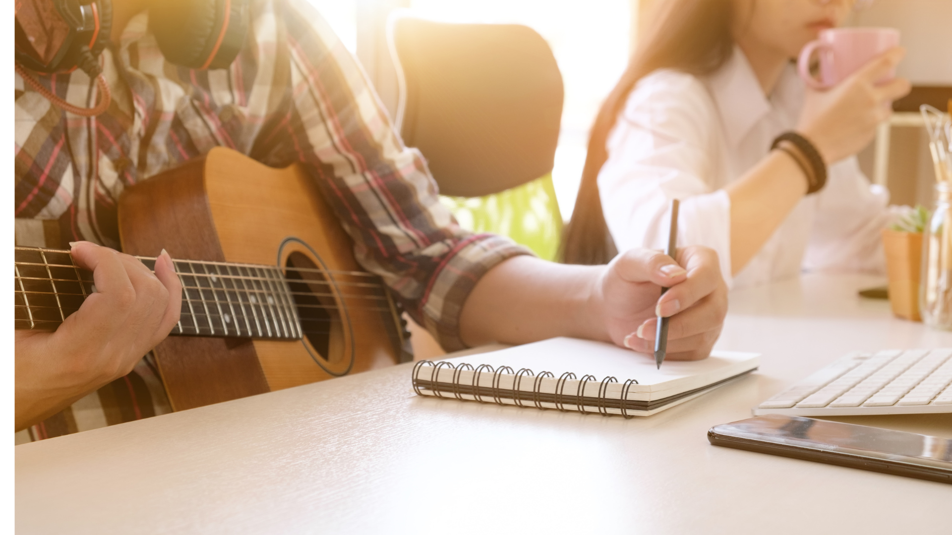 Close-up of a songwriter holding a guitar and writing lyrics in a spiral notebook on a desk. Close-up of a songwriter holding a guitar and writing lyrics in a spiral notebook on a desk.
