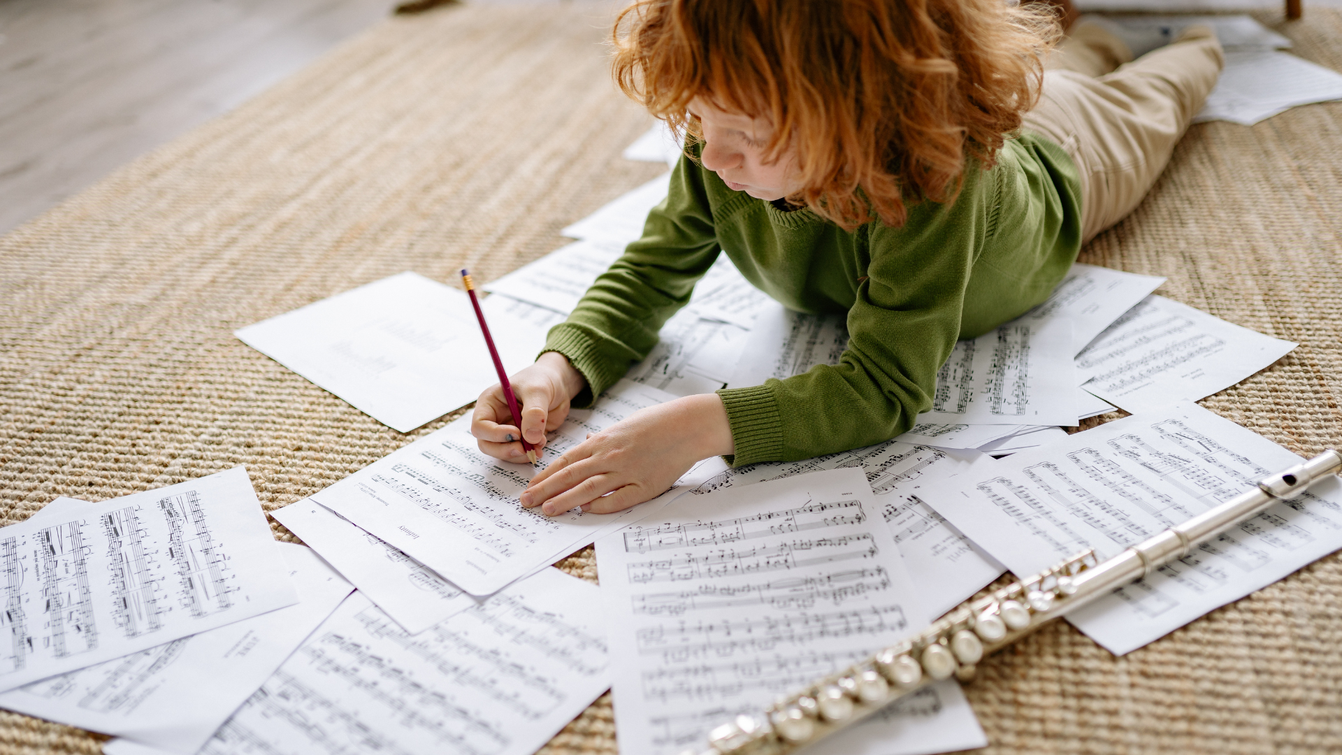 Young child lying on a rug surrounded by sheet music, writing with a pencil, illustrating the start of a songwriting journey. Young child lying on a rug surrounded by sheet music, writing with a pencil, illustrating the start of a songwriting journey.
