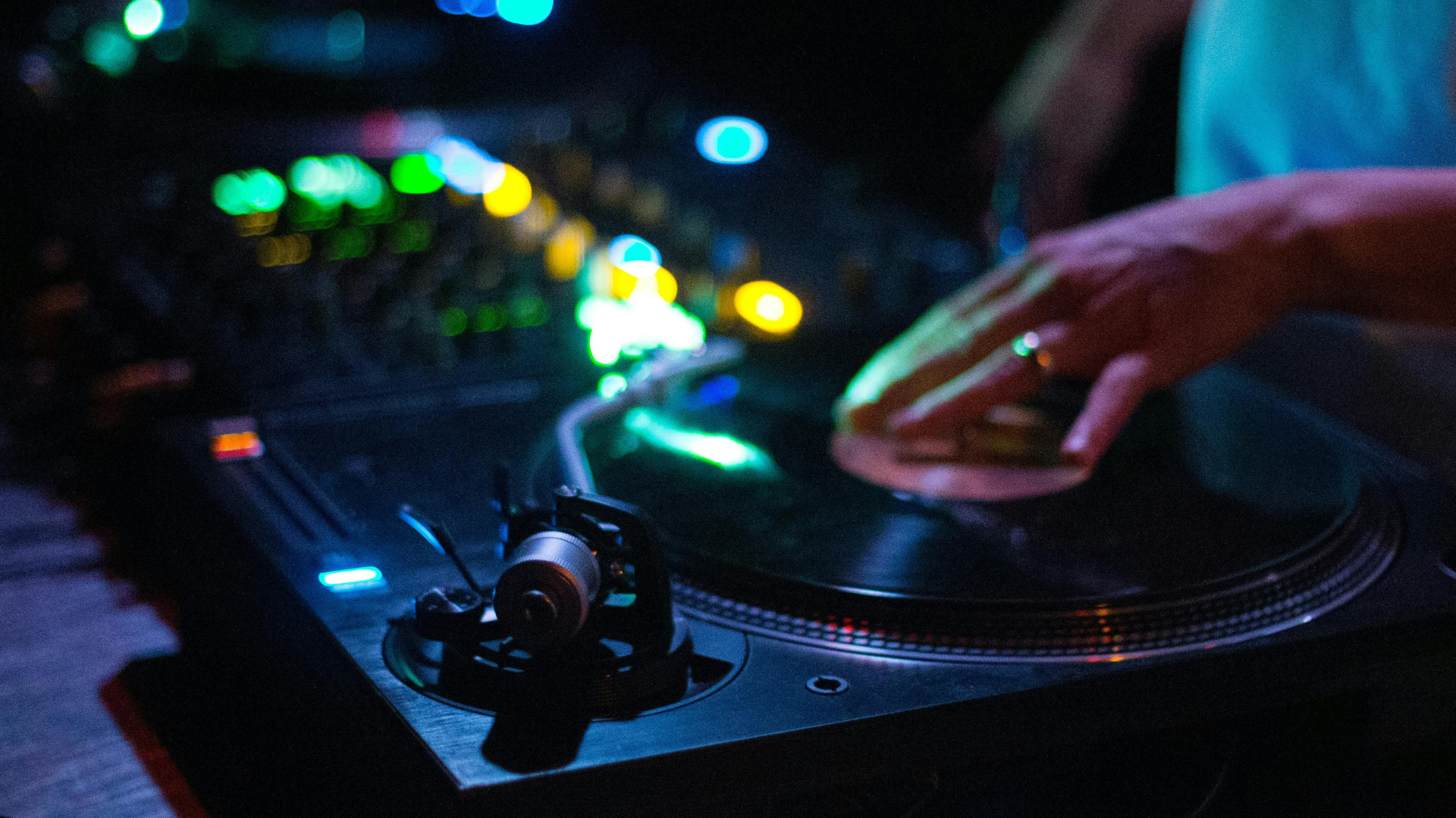 DJ using a turntable in a dark studio or club setting with colorful lights and vinyl playback equipment.