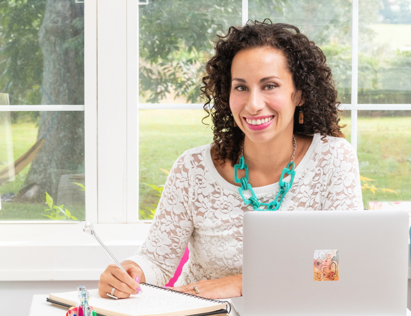 Jules De Jesus Fritz Puerto Rican woman sitting at desk with notebook pen and laptop wearing white shirt and teal necklace