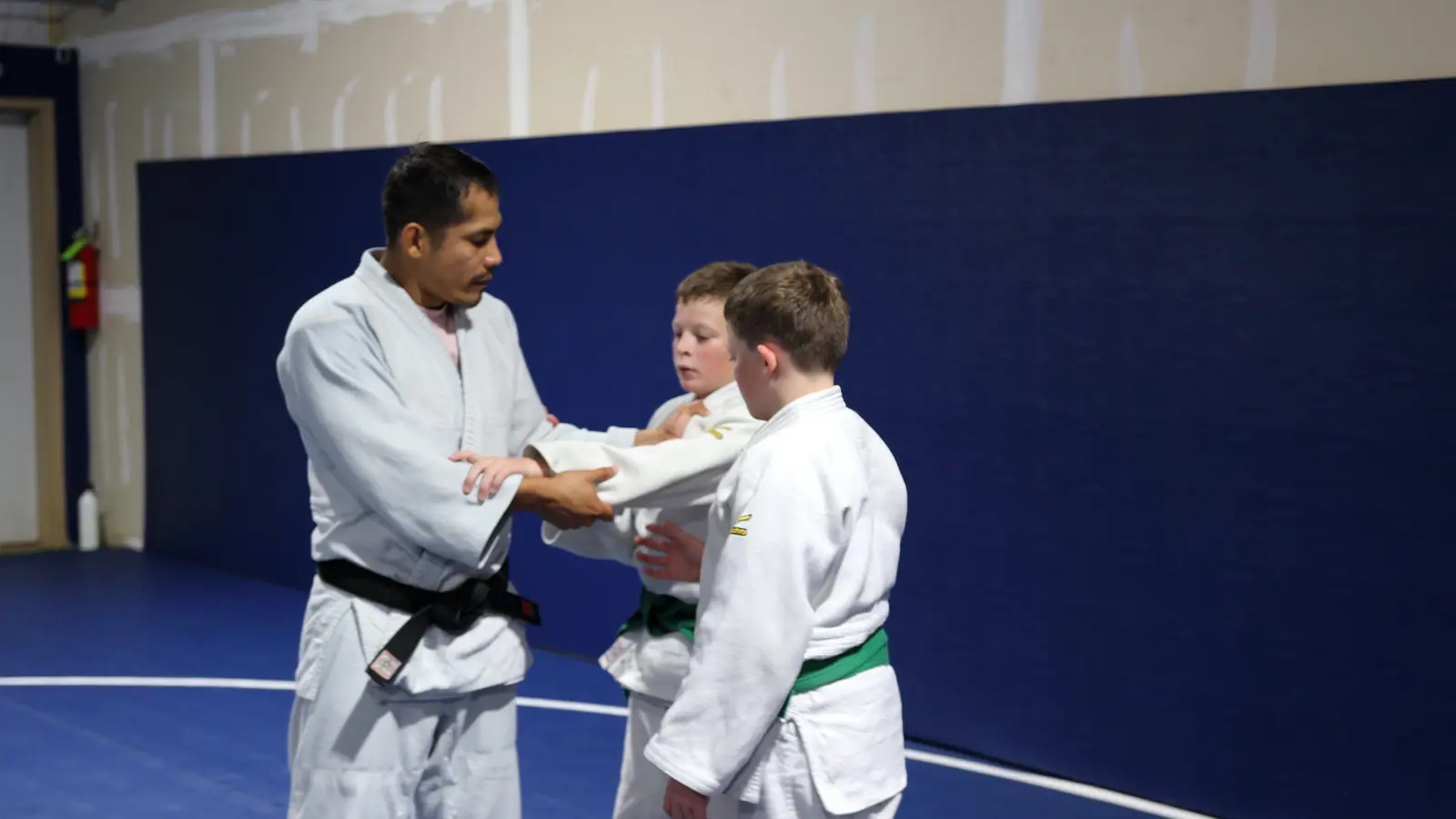 Coach Jhonatan Gutierrez showing young students how to grip a judo gi