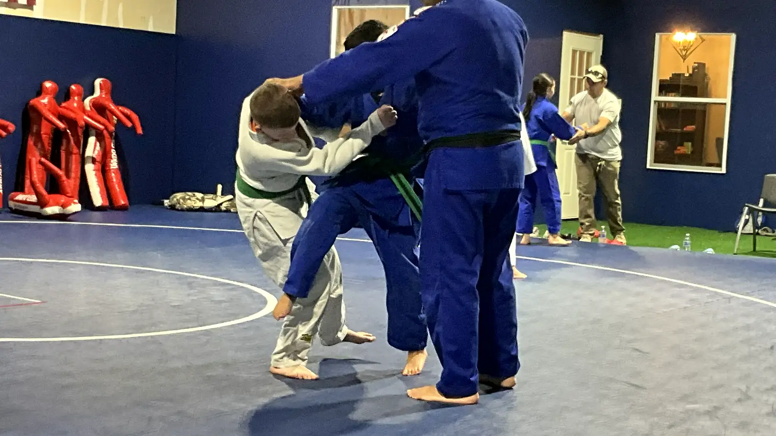 Judo coach in a blue gi guiding a student through a throw