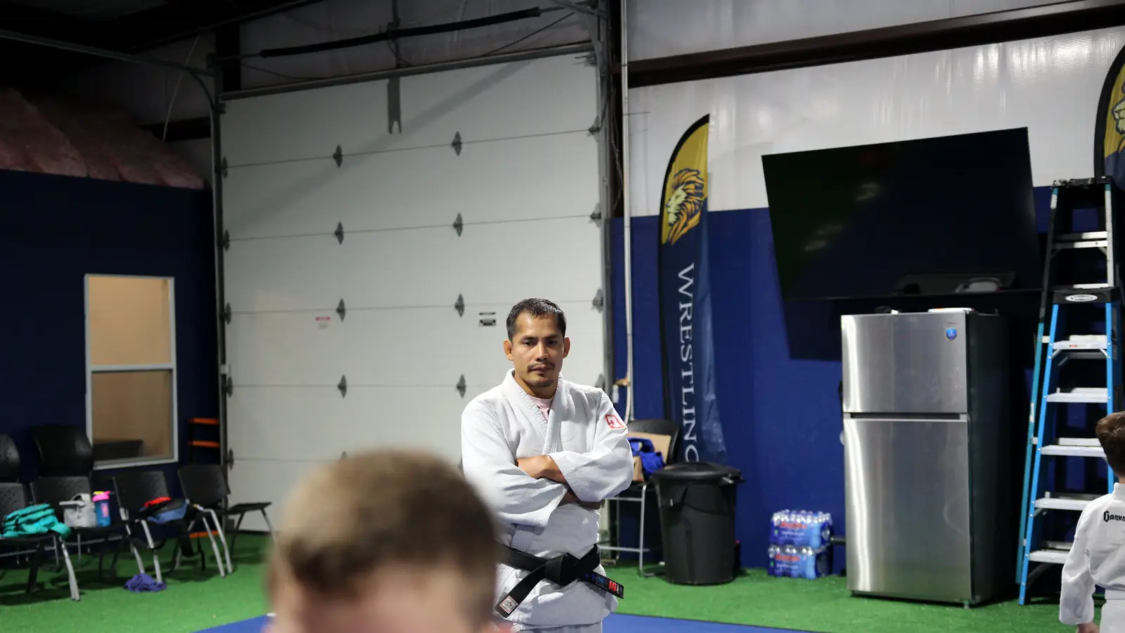 Coach in a white gi with arms crossed, watching students train