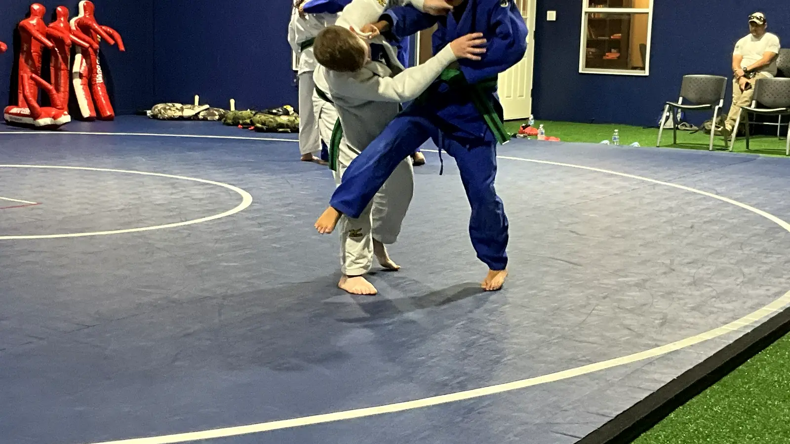 Two kids in white and blue gis practicing a judo foot sweep