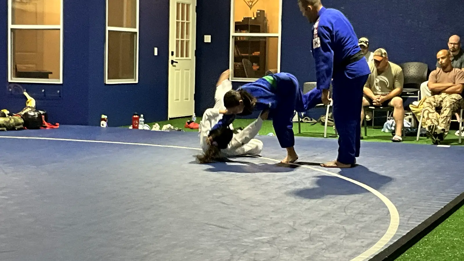 Judo coach closely supervising a student finishing a throw during class