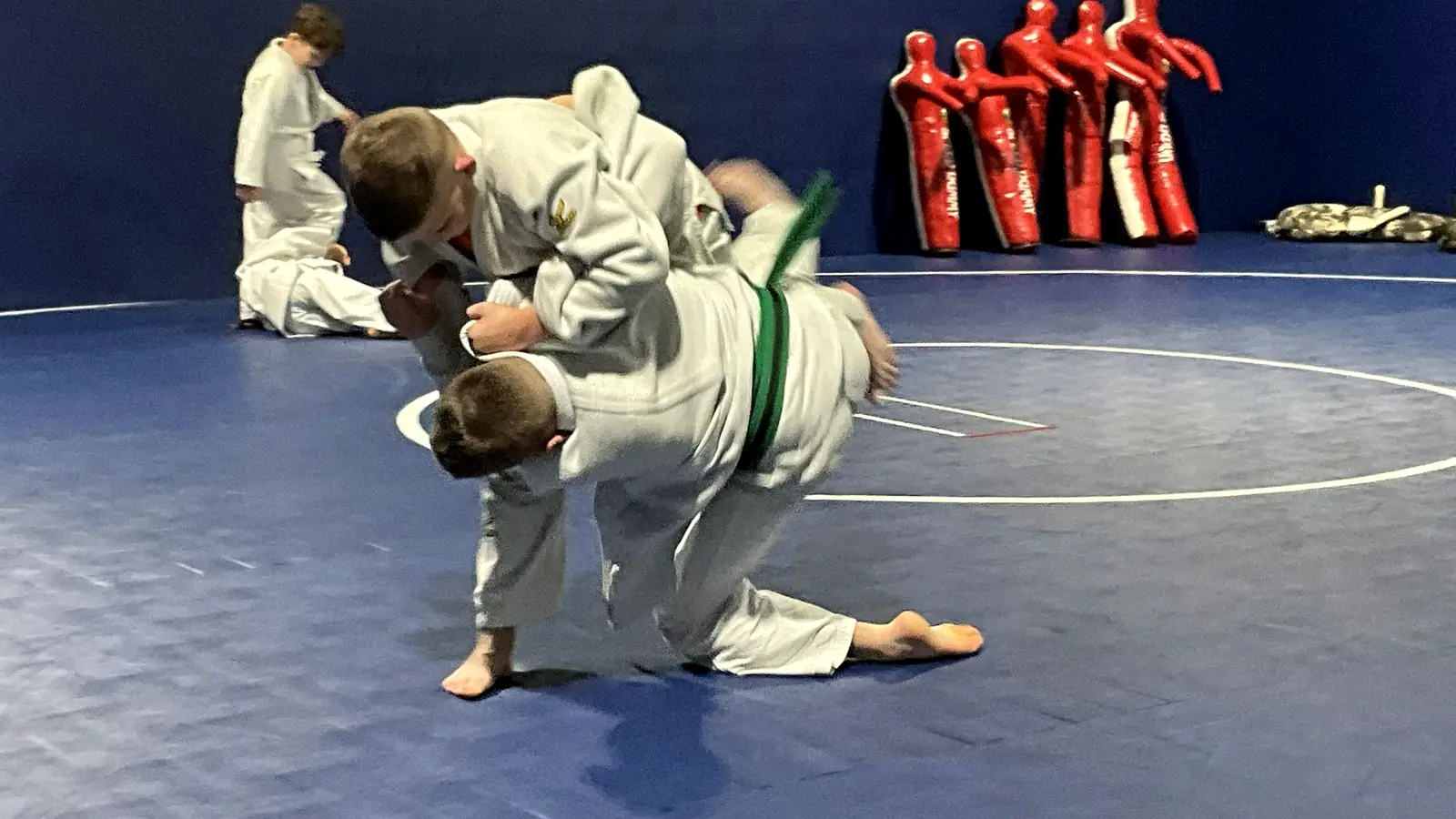 Two young judo students completing a hip throw near the throwing dummies