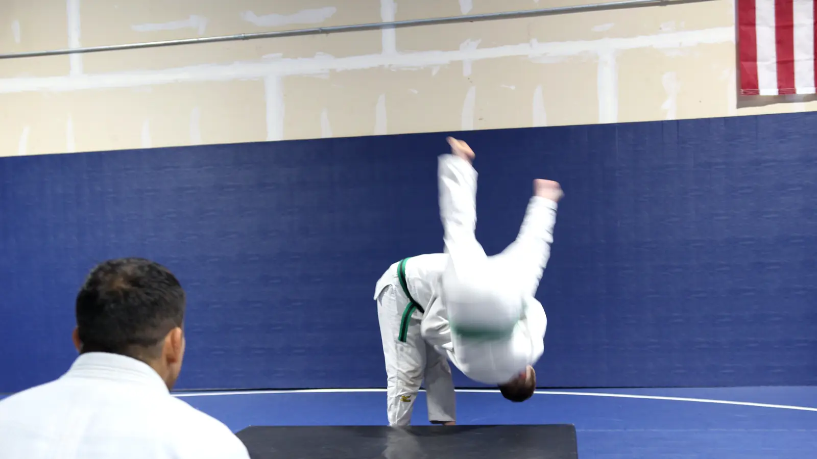 Young judo student thrown through the air onto a crash pad while a coach watches