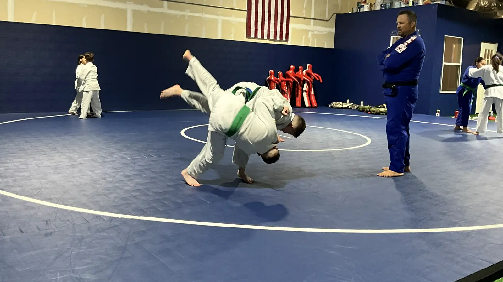 Two youth judo students complete a throw while a black-belt coach watches