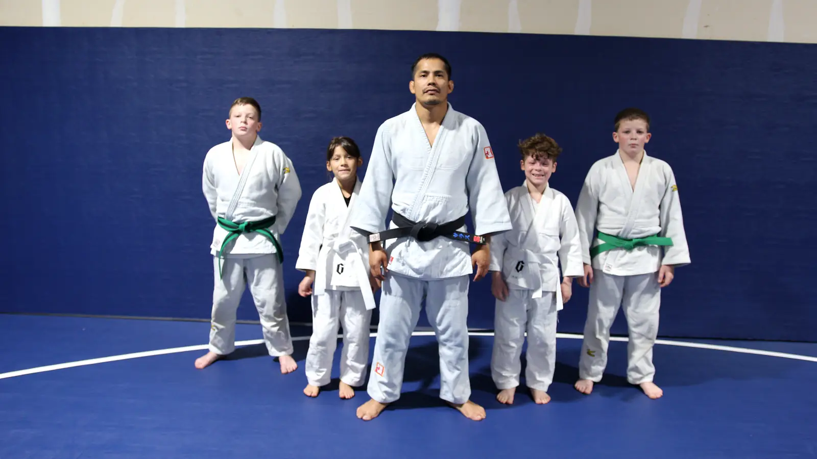 Black-belt coach standing with four youth judo students in white gis