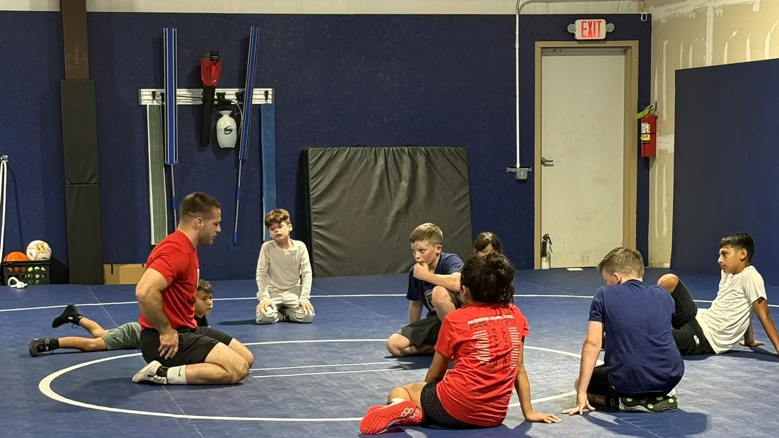 Coach sitting on the mat leading a small group of youth wrestlers through drills