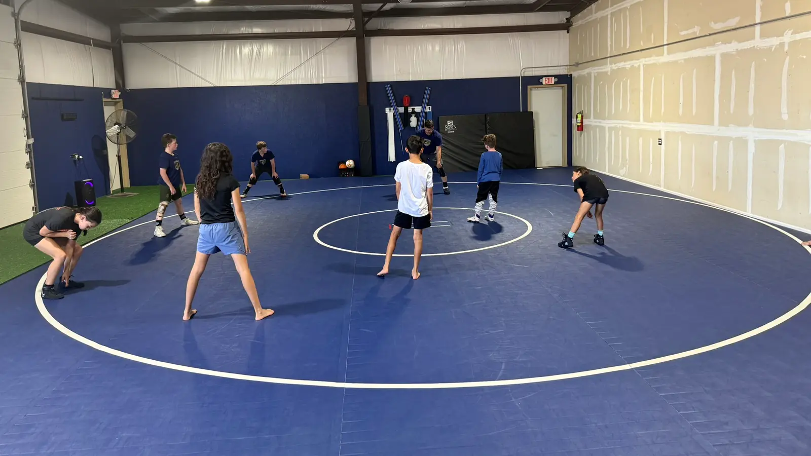 Young wrestlers in stance drilling across the blue mats at Dominion Academy