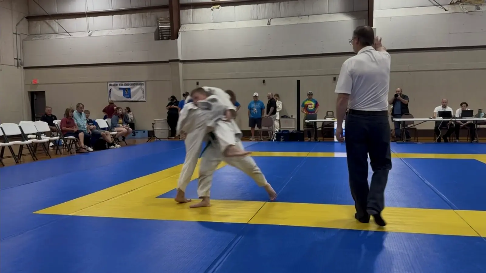 Dominion youth judoka throwing an opponent at a judo tournament while a referee watches