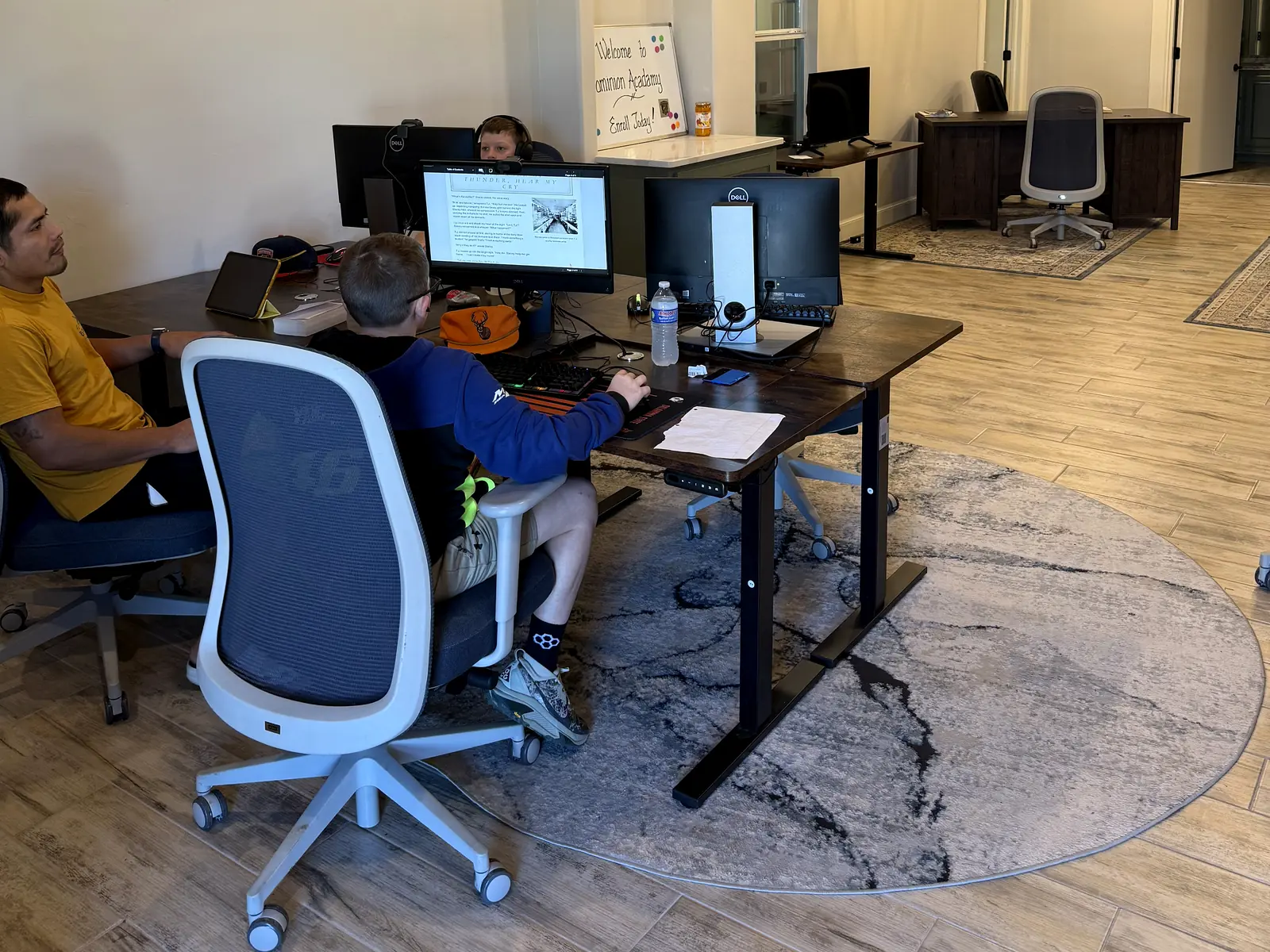 Student working at a computer desk with a coach sitting beside him