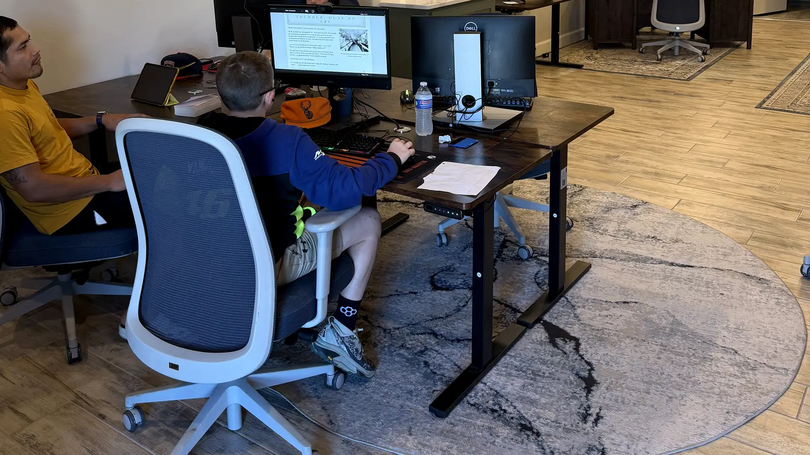 Student focused on online coursework while a coach sits beside him in the study room