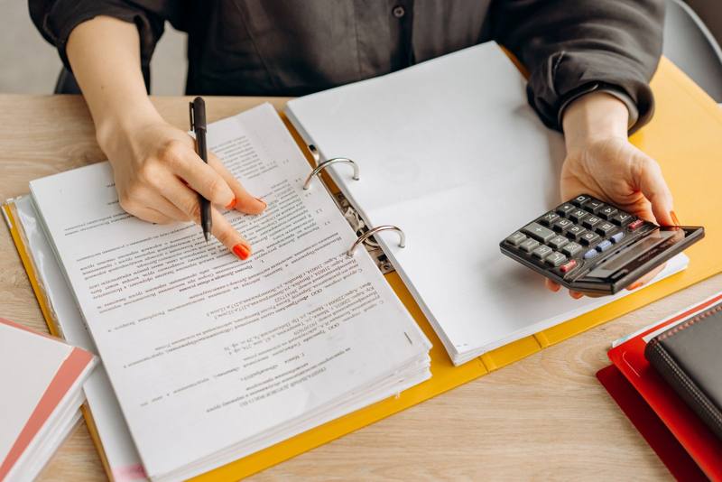 Hands reviewing paperwork with a calculator (stock photo)