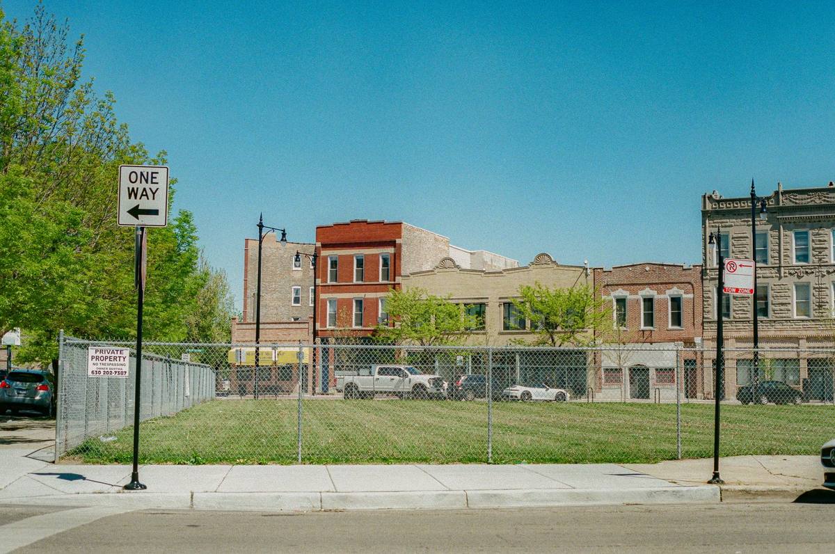 Empty grass lot behind a chain-link fence between buildings (stock photo)