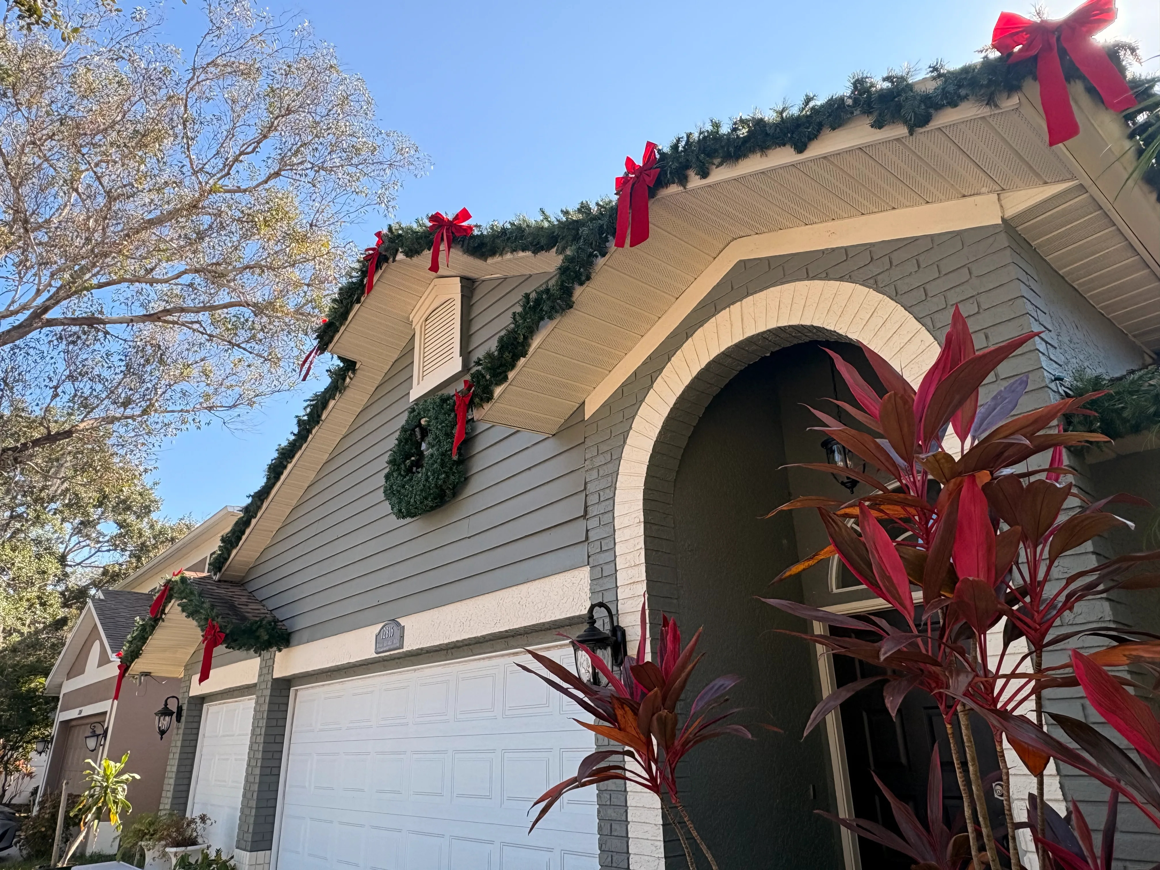 Professional holiday lighting technician working from a ladder along a roofline